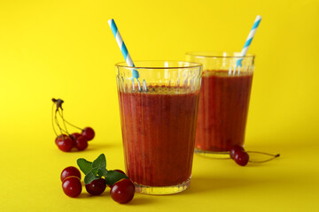 Glasses of cherry smoothie and ingredients on yellow background