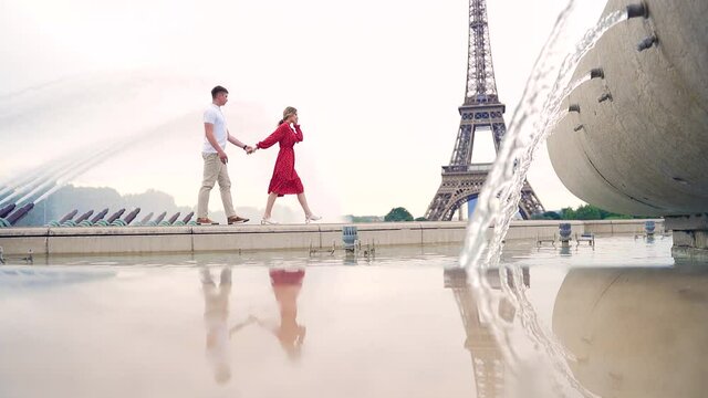 young couple in love walking holding hands in Paris background of the Eiffel Tower. France, Europe. Girl in red dress and guy. Travel tourists on honeymoon. Valentines day Romantic date and meeting