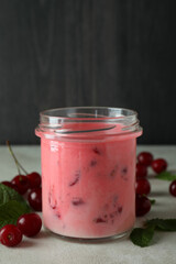 Glass jar of cherry smoothie and ingredients on white textured table