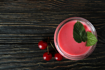 Glass jar of cherry smoothie and ingredients on rustic wooden table