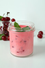 Glass jar of cherry smoothie and ingredients on white background
