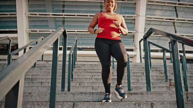 Intense cardio training. Young active overweight african american woman running on staircase, going down stairs alone
