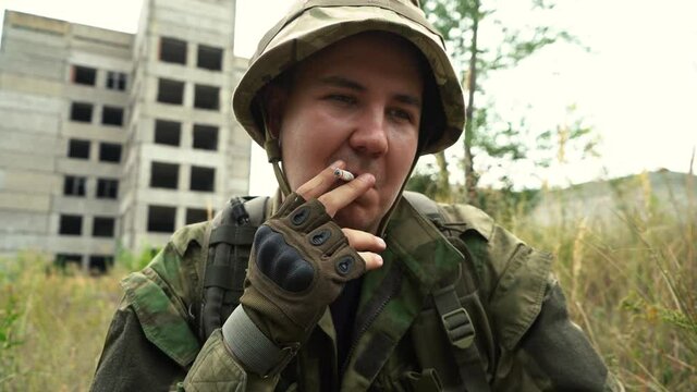 man in uniform smokes a cigarette while sitting on the ground