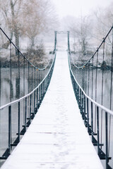 Pedestrian suspension bridge made of steel and wood across the river, winter