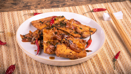 Spicy fried tofu with onions in a plate with chopsticks, close-up