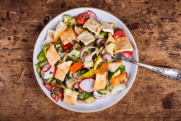 Traditional vegetarian Arabic fattoush salad with vegetables and pita in a plate, top view
