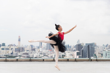 Fototapeta na wymiar Asian ballerina ballet girl in red, black dress dancing on rooftop with cityscape view background. Young ballerina ballet girl dancing by stretching arms and leg on rooftop