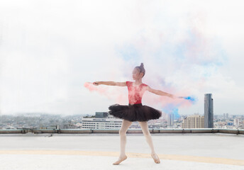Asian ballerina ballet girl dancing with colour smoke on rooftop and skyscraper city view background. Female ballet dancer practicing dancing. Young ballerina ballet girl dancing