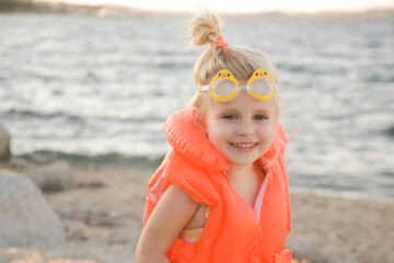 Toddler girl in orange life jacket vest with water behind