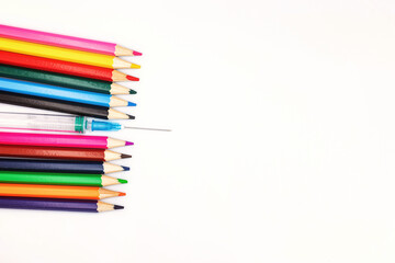 An empty syringe with a needle lies among colored pencils