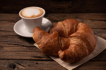 Fresh buttery croissants with coffee on rustic wooden table