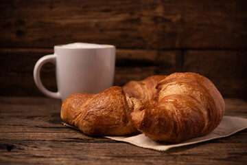 Fresh buttery croissants with coffee on rustic wooden table