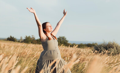 beautiful pregnant woman walks in field among dry fluffy grass enjoying sunset, relaxation on summer nature, preparation for childbirth and happy, healthy motherhood