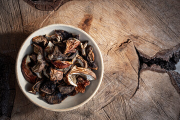 Freshly dried boletus mushrooms in a ceramic bowl. Food on a piece of wood. Organic vegetarian diet ingredient. Selective focus on the details, blurred background.