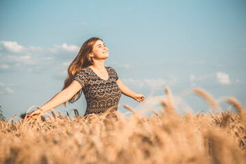 romantic young woman enjoying nature, raising hands on background of cloudy sky in wheat field, girl breathe breathes deeply, freedom and relaxation concept