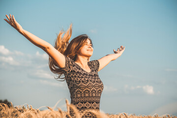 happy beautiful young woman enjoying nature, raising hands on background of cloudy sky in wheat field, girl breathe breathes deeply, freedom and relaxation concept © fantom_rd