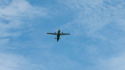 View of propeller plane flying low with blue sky and clouds at background.