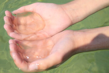Girl catches jellyfish with her hands in sea water. The sandy bottom is visible through the clear water. 