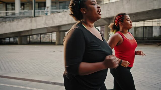 Sport in your life. Active overweight african american women running together in urban area, practicing cardio workout