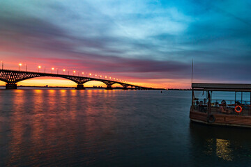 Fototapeta na wymiar Night river before beautiful sunrise. Sunrise on river under dramatic sky. Light on bridge.