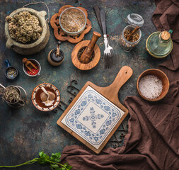 Various rustic aged kitchen utensils on dark table background with chopping board, forks and dried condiments. Top view