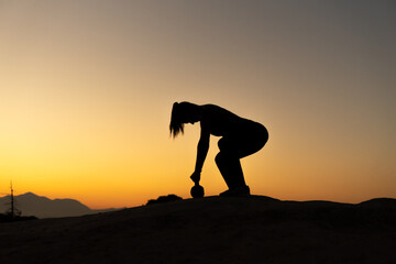 Silueta de deportista entrenando con un kettlebell en la montaña, con el atardecer y espacio para texto. 