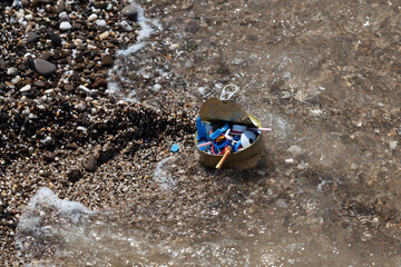 Naklejka premium Plastic garbage and tin can on seashore. Household waste and disposable plastic waste on beach. Sea wave, microplastics in world ocean