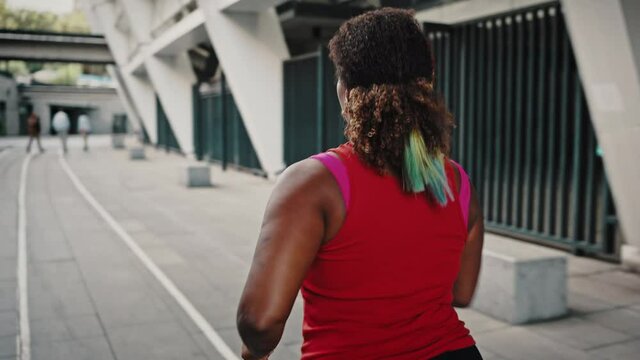 Close up portrait of young chubby african american woman running alone in urban training area, tracking shot