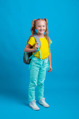 a little girl with a backpack holds a book on a blue background