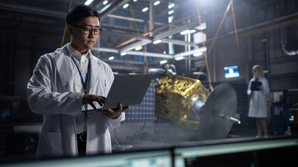 Industrial Engineer Working on Artificial Satellite Construction. Aerospace Agency: Asian Scientist Using Laptop Computer to Develop Spacecraft for Space Exploration and Data Communication.