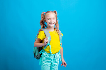 happy  little girl with a backpack holds a book on a blue background