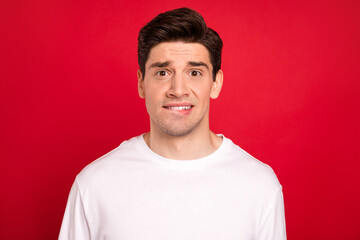 Photo of sad brunet millennial guy bite lip wear white shirt isolated on red color background