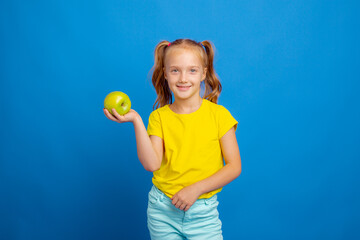 Fototapeta na wymiar a little girl holds an apple on a blue background
