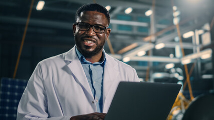 Industrial Engineer Working on Artificial Satellite Construction and Smiling on Camera. Aerospace Agency: African American Scientist Using Laptop Computer to Develop Spacecraft for Space Exploration.