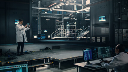 Male Engineer Uses Tablet Computer while Working in an Industial Facility at a Factory. Scientist uses Augmented Reality Software. Empty Space Left for Mock Up Template for VFX.