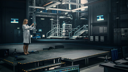 Female Engineer Uses Tablet Computer while Working in an Industial Facility at a Factory. Scientist uses Augmented Reality Software. Empty Space Left for Mock Up Template for VFX.