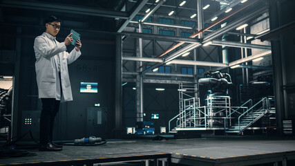 Male Engineer Uses Tablet Computer while Working in an Industial Facility at a Factory. Scientist uses Augmented Reality Software. Empty Space Left for Mock Up Template for VFX.