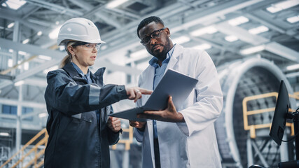 Fototapeta na wymiar Team of Diverse Professional Heavy Industry Engineers Wearing Safety Uniform and Hard Hat Working on Laptop Computer. African American Technician and Female Worker Talking on a Meeting in a Factory.