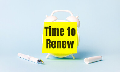 On a light blue background - a white handle and an alarm clock with a bright yellow sticker glued to it with the text TIME TO RENEW