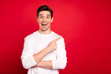 Photo portrait brunet guy in white shirt blue jeans amazed smiling showing copyspace isolated vibrant red color background