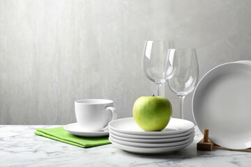 Set of clean dishware, glasses and apple on white marble table, space for text