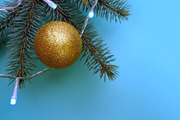 on the Christmas tree there is a shiny round golden Christmas toy with a garland on a blue background . top view . Christmas time
