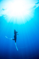 Fototapeta na wymiar Young freediver asian woman with fins glides and amazing sun rays. Freediving underwater in Amed, Bali Indonesia. 