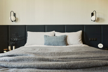Stylish composition of small modern bedroom interior. Bed, creative lamp and elegant personal accessories. Walls with black panels. Minimalistic masculine concept. Details. Template.