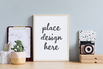 Creative composition of stylish home office workspace with mock up poster frame, succulent, camera and office accessories. Light and cozy space. Neutral colors. Template.