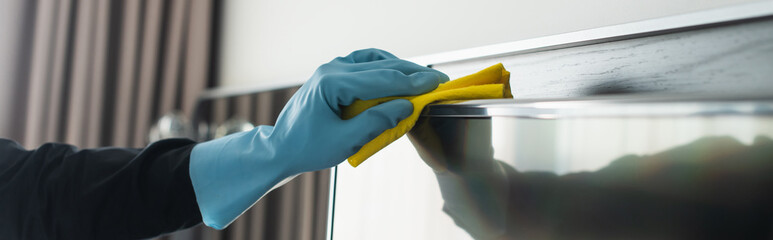 partial view of housekeeper in blue rubber glove cleaning tv display with rag, banner