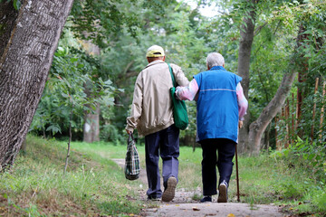 Elderly couple walking in a park holding hands. Old man holds woman with cane by the arm, life in retirement