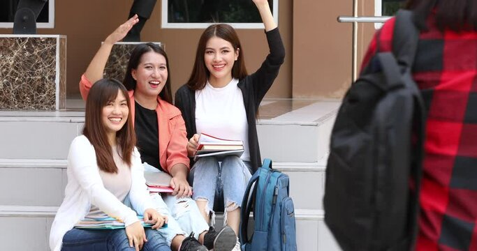 College close friends sitting together on school building downstairs before class and then looking another group members walking then they rise hands to say hello and invite to join.