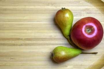 Two small green juicy pears and one large red ripe apple are lying on wooden platter. Top view. Close-up. Copy space. Healthy food, diet. Selective focus.