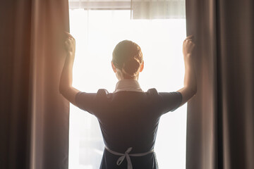 back view of maid adjusting curtains in hotel room - obrazy, fototapety, plakaty